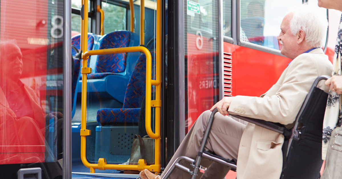 Senior gentleman in wheelchair being wheeled onto accessible bus by his wife