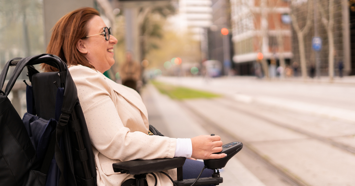 Woman smiling in power wheelchair outside waiting to cross the street