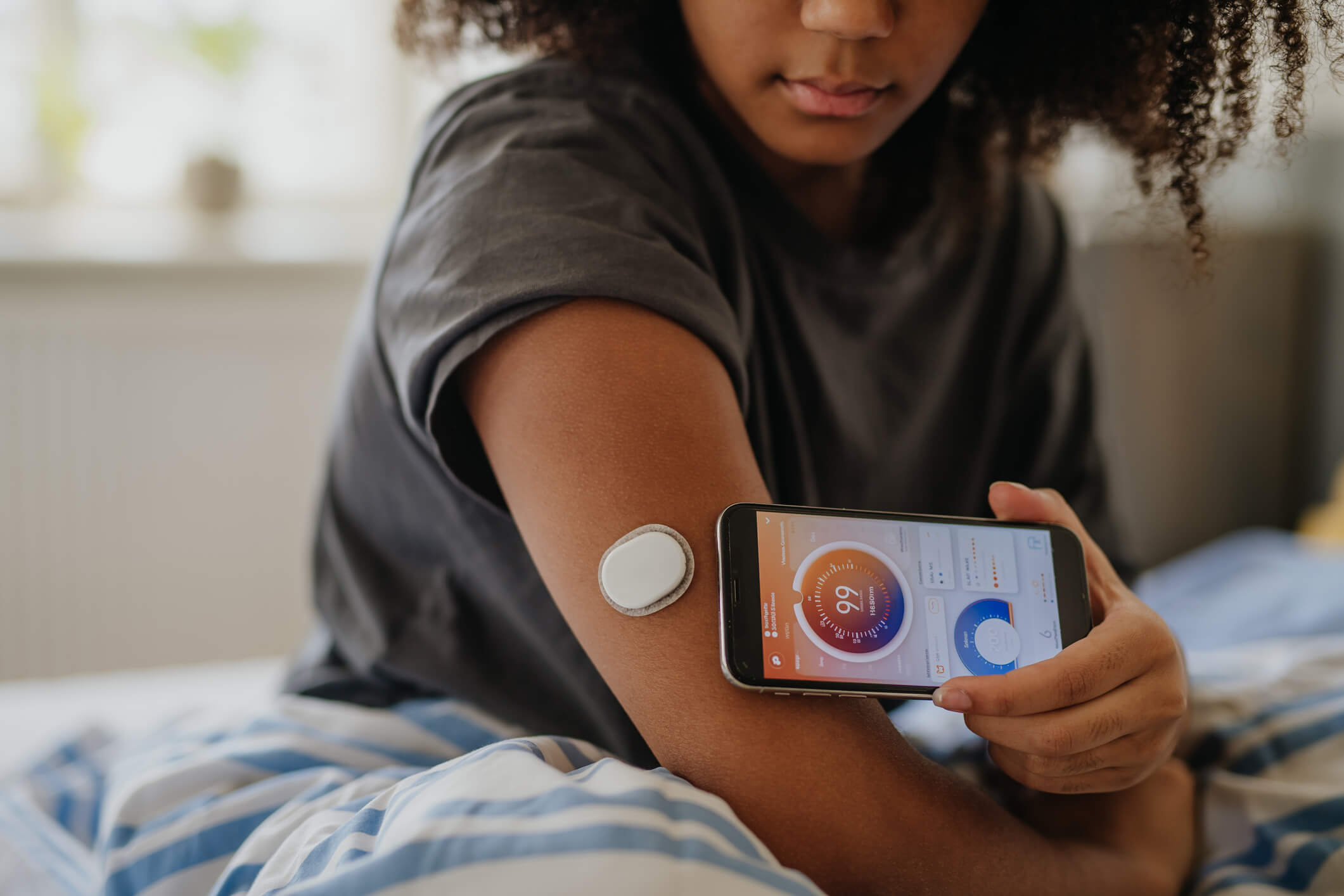 Teenage girl connecting smartphone to continuous glucose monitor, checking blood glucose first thing in the morning.
