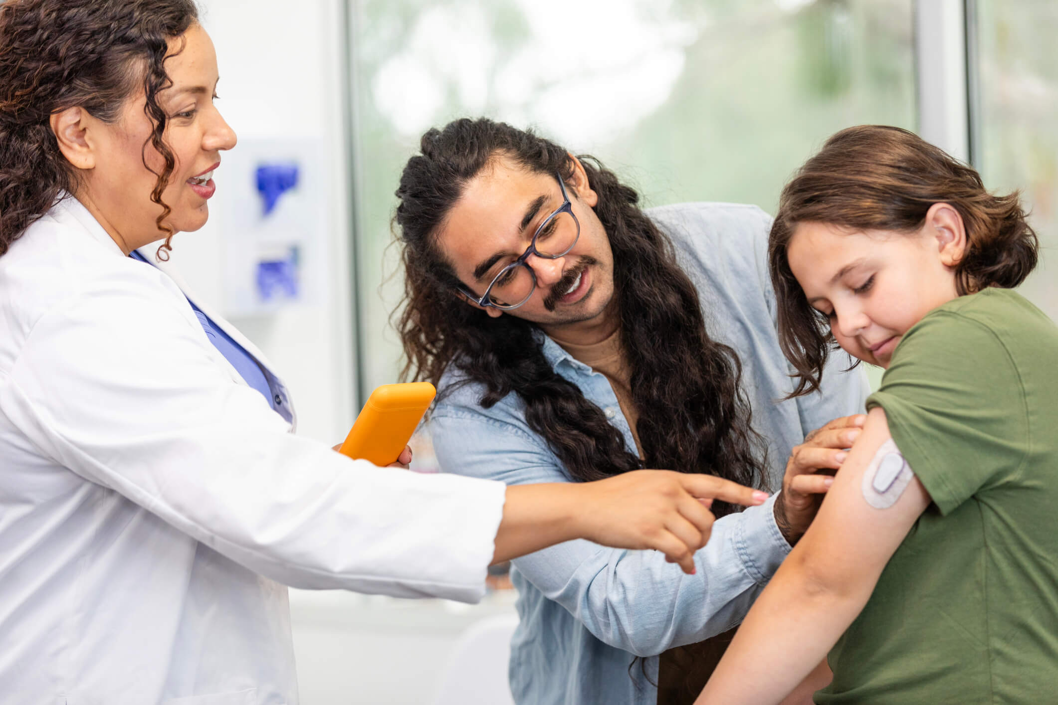 Female doctor teaches father and son about glucose monitor.
