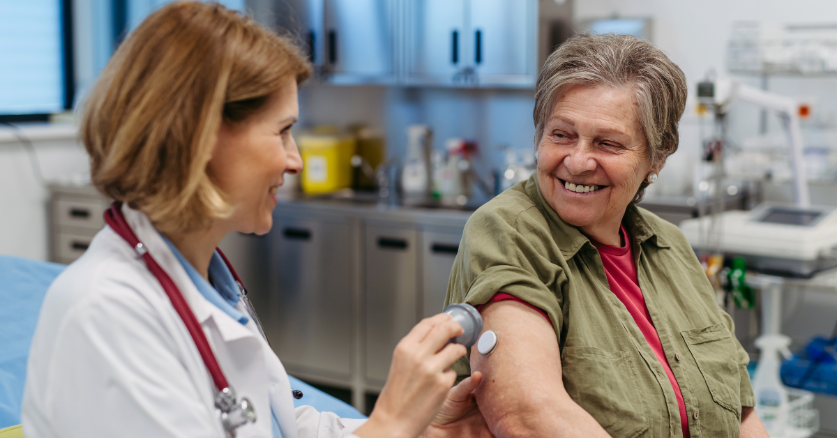 Female doctor smiling while applying CGM to arm of smiling senior female patient