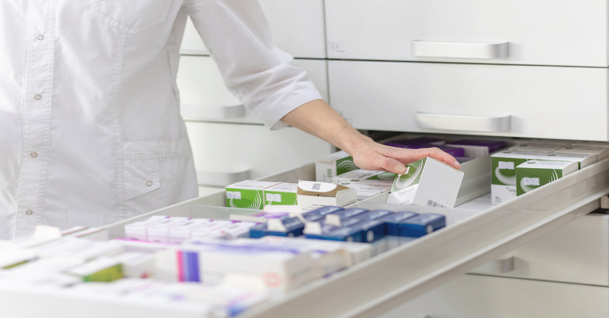 A pharmacist in a white shirt browses through a long drawer full of different medical supplies in their own boxes.
