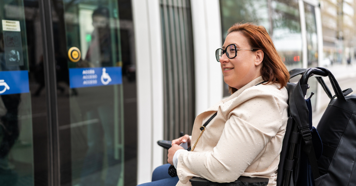 Smiling woman in power chair waiting outside for accessible public transport