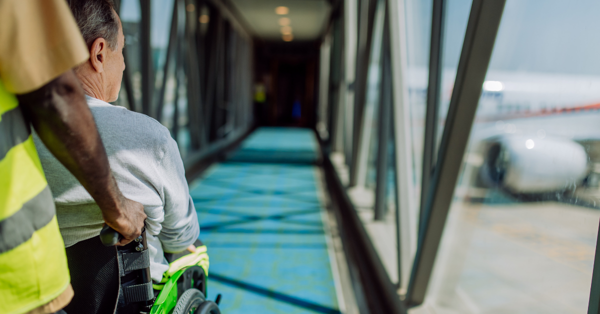 Man in power chair being transported to airplane by airport worker