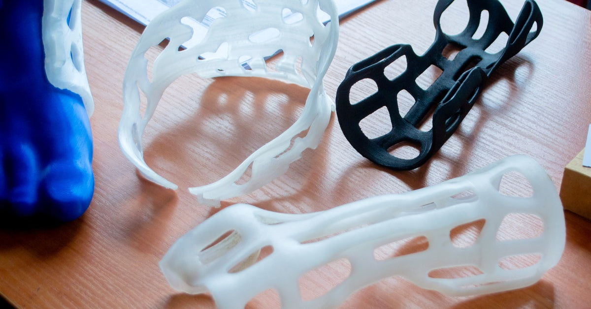 Three 3D-printed parts of a custom leg prosthetic lying on a wooden table next to some paperwork.