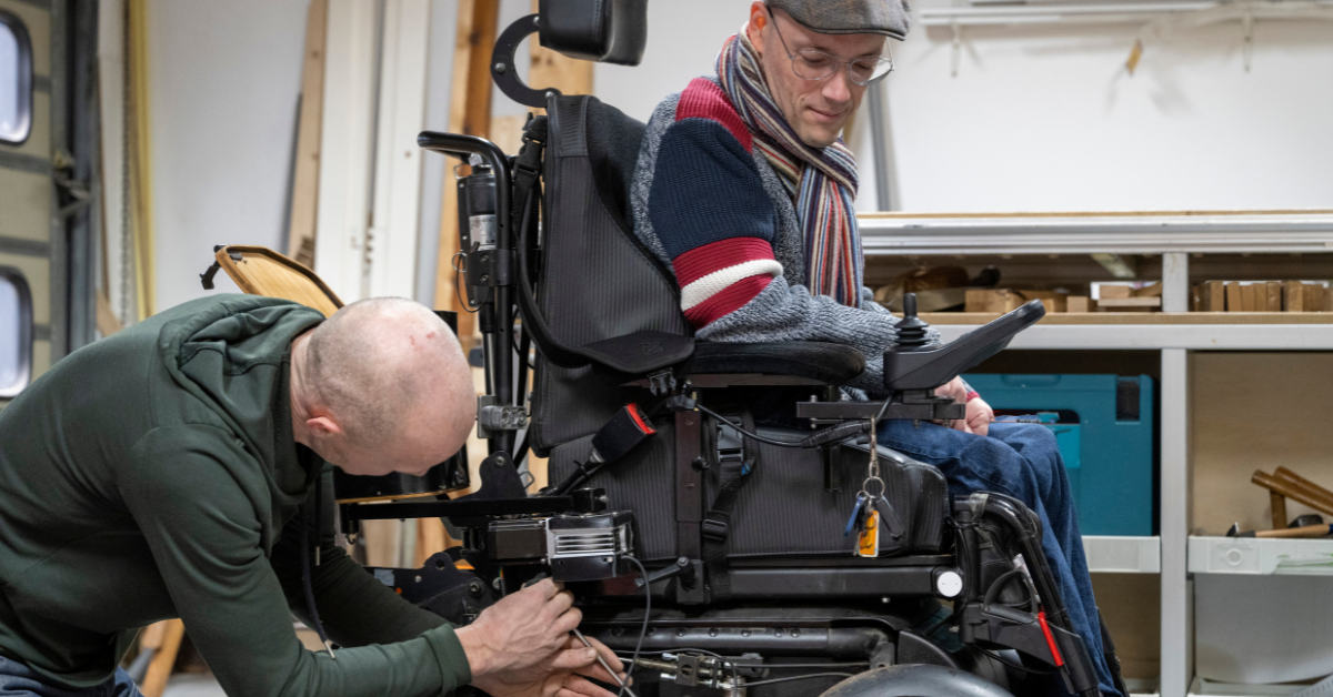 Technician checking man's power wheelchair battery while he is seating in the chair