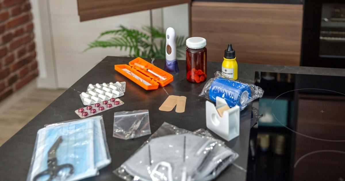 A collection of medical supplies laid out on a kitchen table. It includes masks, pills, scissors, and bandages.