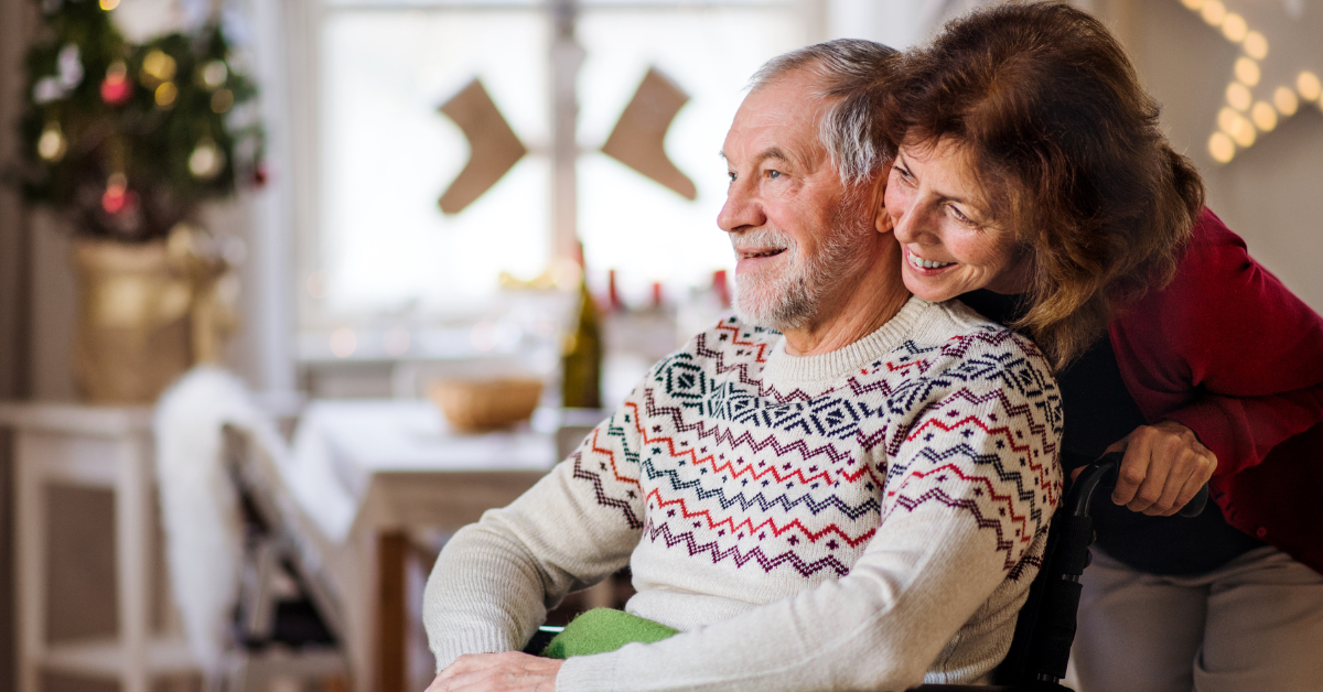 Man in wheelchair smiling as his wife leans over next to him