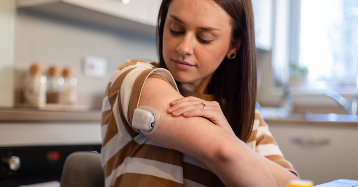 Woman looking at the continuous glucose monitor on her arm while seated at her kitchen table