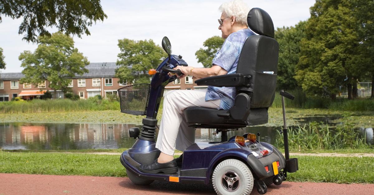Senior woman riding on dark blue power mobility scooter by sidewalk near water