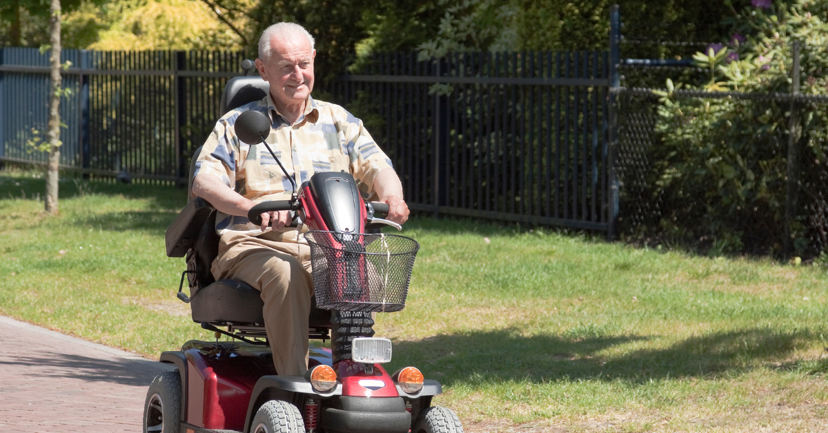 Senior man smiling and riding on a red mobility scooter outside