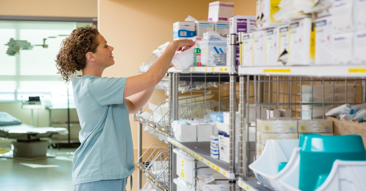A woman wearing scrubs looks at some different varieties of medical supplies sitting on some shelves.